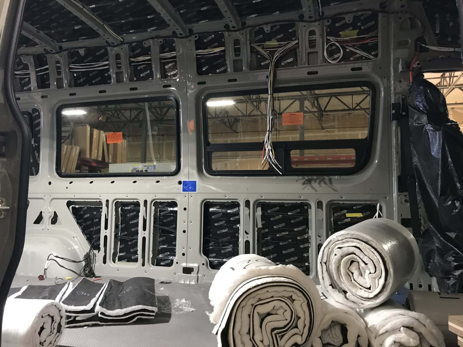 An empty Sprinter cargo van with exposed wires and rolls of sound dampening material